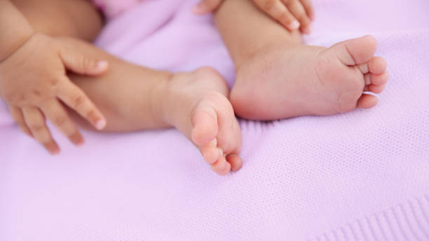 Baby girl sitting on pink blanket with barefeet, closeup of tiny feet stock photo