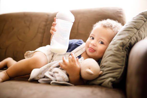 Baby holding milk bottle Baby suckling milk bottle lying on sofa baby formula stock pictures, royalty-free photos & images