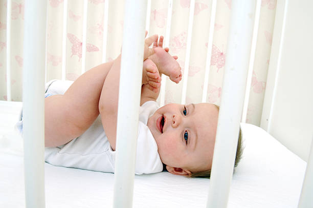 Baby holding their toes while lying in crib stock photo