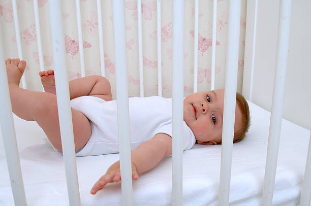 Baby in white lying on back in a white crib stock photo