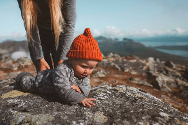 Baby learning crawling outdoor family vacation mother with child infant  wearing orange hat autumn season in Norway stock photo