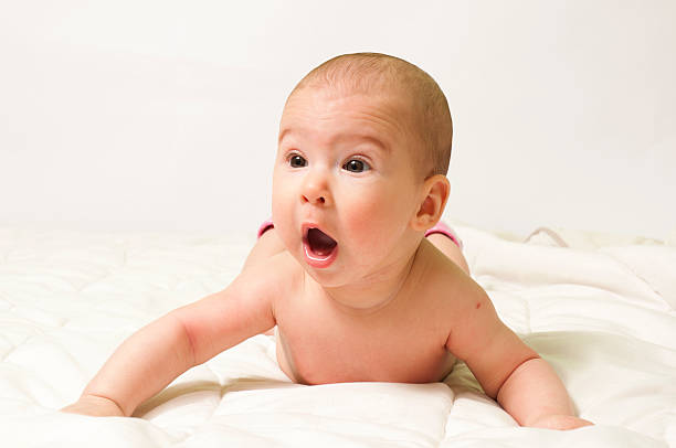 Baby lying on stomach on quilt with mouth open stock photo