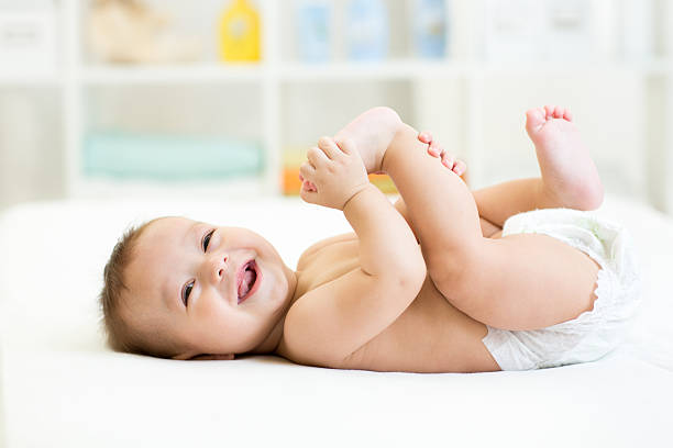 baby lying on white bed and holding legs stock photo