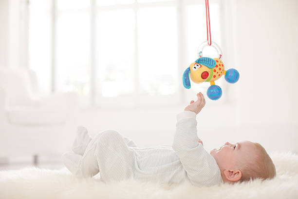 Baby on rug reaching for hanging toy overhead  babies only stock pictures, royalty-free photos & images