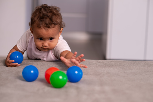 Portrait of a smiling infant playing with colorful plastic balls.