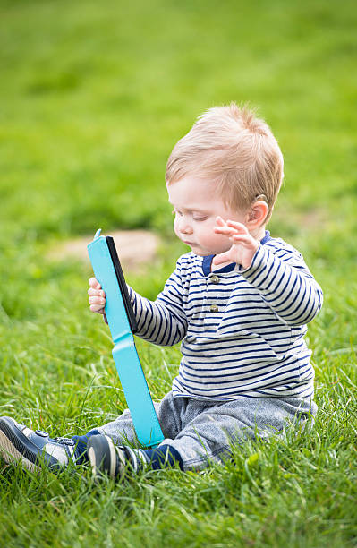 Baby sitting on a lawn and playing  with smart phone stock photo