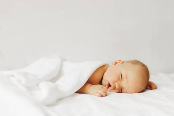 Baby sleeps on the bad. Beautiful baby sleeps on the bed in white sheets. baby stock pictures, royalty-free photos & images