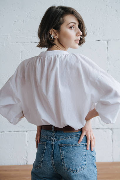Back image of a young woman looking to side. She wears shirt and jeans stock photo