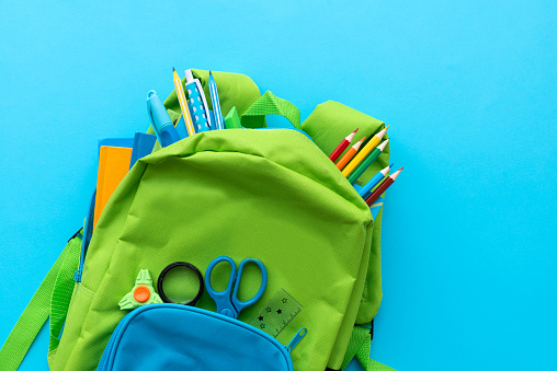 Back to school concept. Backpack with school supplies on blue background. Top view. Copy space