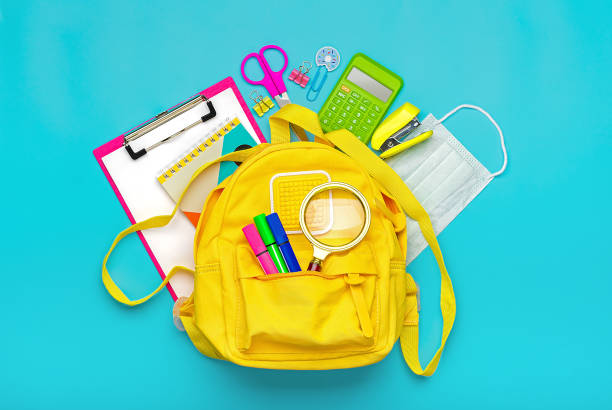 back to school, education concept yellow backpack with school supplies, protective medical mask, calculator, scissors isolated on blue background. top view copy space flat lay - back to school imagens e fotografias de stock