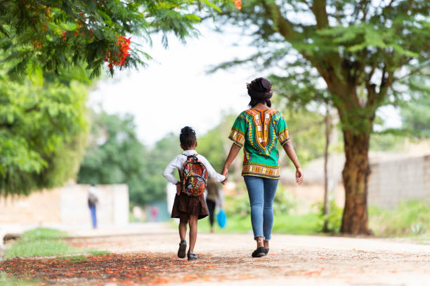 Back view mother walking daughter to school on rural road stock photo