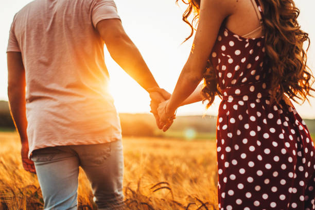 Back view of a couple in love walking on the meadow. Man and woman in love holding hands. stock photo