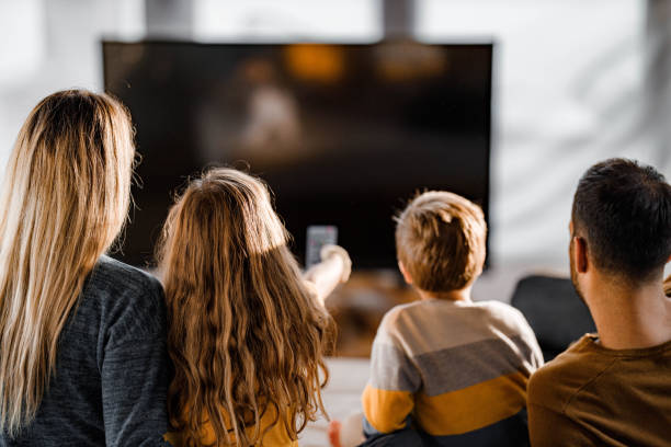 Back view of a family watching TV at home. Rear view of a relaxed family watching a movie in the living room. watching tv stock pictures, royalty-free photos & images