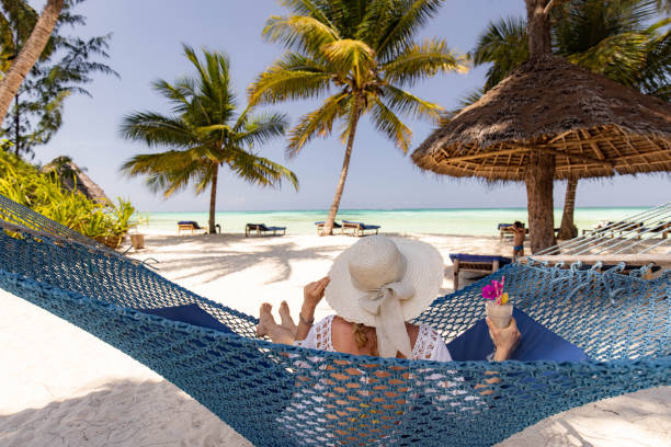 Back view of a relaxed woman with smoothie in hammock on the beach. stock photo