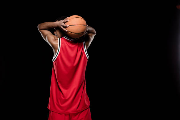 achteraanzicht van afro-amerikaanse basketballer gooien van de bal op zwart - basketball player back stockfoto's en -beelden