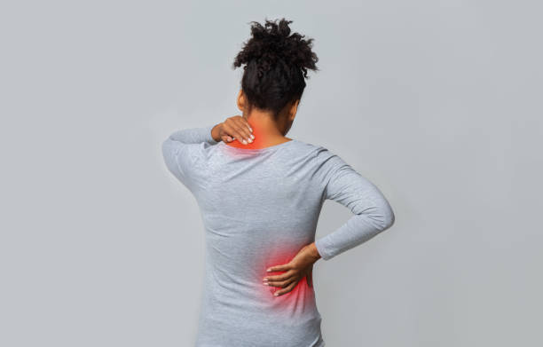 Back view of afro woman rubbing her neck and loins Back view of african woman rubbing her inflamed neck and loins, grey background osteoporosis photos stock pictures, royalty-free photos & images