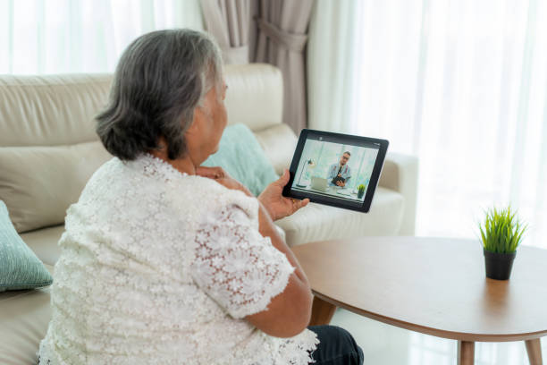 назад зрения пожилая женщина делает видео-звонок со своим врачом с ее чувство боли в горле на цифровой планшет онлайн здравоохранения цифр� - at home covid test стоковые фото и изображения