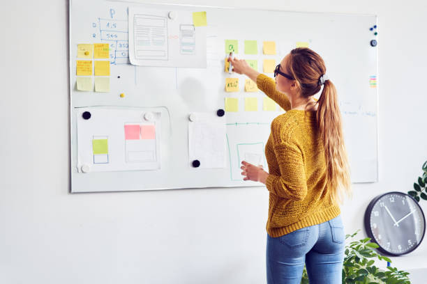 Back view of female web designer working on whiteboard in office stock photo