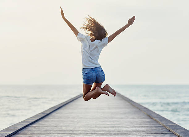 back view of jumping girl on the pier - alegria imagens e fotografias de stock