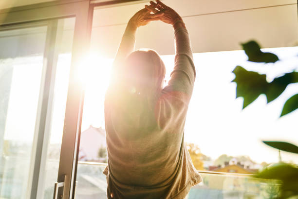 Back view of senior woman stretching in the beams of the sun stock photo