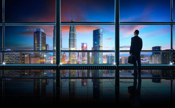 achteraanzicht van doordachte zakenman kijken uit grote office-venster op kantoor - business malaysia stockfoto's en -beelden