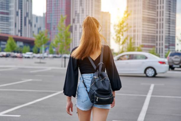 Back view of walking fashionable teenage girl with backpack stock photo