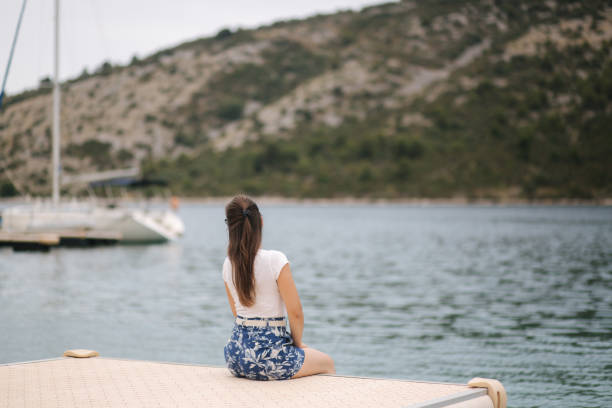 achteraanzicht van de vrouw zitten op de pier aan de zee. prachtige zee - fluisterboot stockfoto's en -beelden