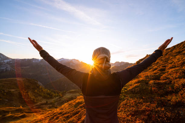 back view woman with arms wide open in mountain sunset freedom, happiness, closeness to nature, rear view upper body woman with outstretched arms standing high up on alpine mountain pasture enjoying sunset over mountain range in autumn, star shapped sun motivation stock pictures, royalty-free photos & images
