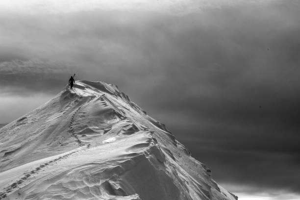 Backcountry skier hikes up snowy mountain peak stock photo