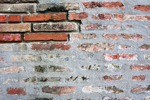 Background of a historical wall made of bricks, the joints of which are partly plastered, but at one point the bricks stand out and stand out.