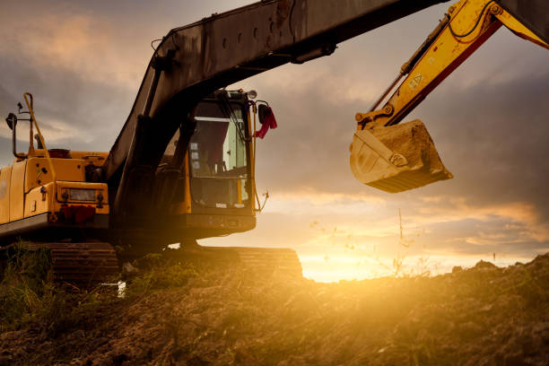 Backhoe at construction site digging soil with bucket of backhoe. Bulldozer on sunset sky. Digger parked at construction site. Earth moving machine. Digger with bucket. Backhoe bucket loading soil. stock photo