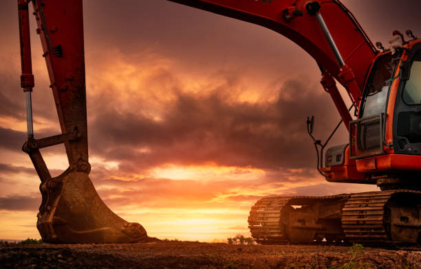 Backhoe parked at construction site after digging soil. Bulldozer on sunset sky and clouds background. Digger after work. Earth moving machine at construction site at dusk. Digger with old bucket. stock photo
