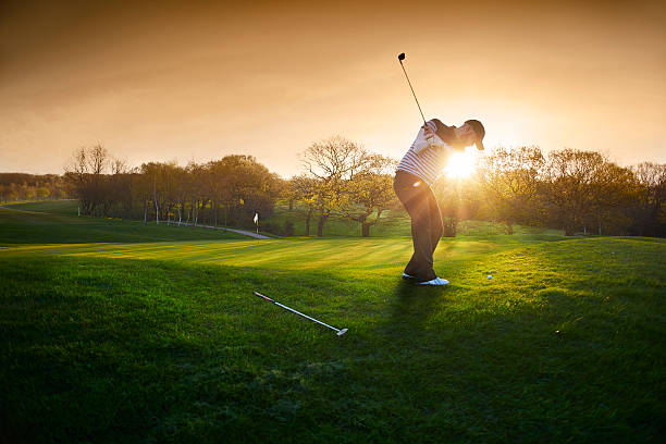 backlit golf course with golfer chipping onto green a lone golfer chips onto the green , the low sun is coming from behind him and flaring to camera. panoramic photos stock pictures, royalty-free photos & images