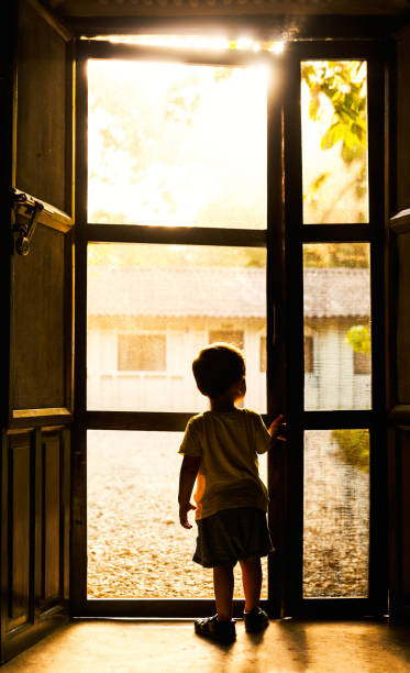 Backlit toddler standing in front of door Backlit toddler standing in front of mosquito net door in Chitwan, Nepal terai stock pictures, royalty-free photos & images