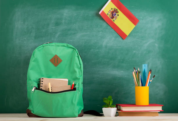 backpack, flag of the Spain, books and school supplies on the background of the blackboard stock photo