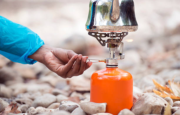 Backpacker tourist's hand regulating gas flame of camping stove. Close up backpacker woman's hand adjusting gas flame regulator of camping stove for outdoor backpacking with piezoelectric ceramic ignition. camping stove stock pictures, royalty-free photos & images