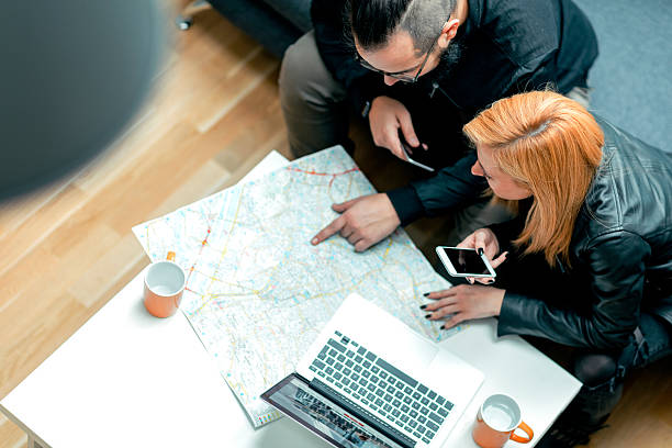 Backpackers Looking For Apartment Online. Young Hipster Couple, backpackers looking on their laptop to rent apartment using vacation home rental services online. Looking at map and laptop. Top view. person looking at map stock pictures, royalty-free photos & images