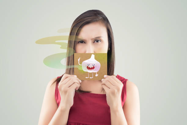 Bad breath or Halitosis Asian woman in the red shirt holding a brown paper white the garlic cartoon picture of his mouth against the gray background, Bad breath, The concept with healthcare gums and teeth bad breath stock pictures, royalty-free photos & images