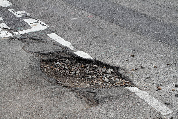Bad repair pothole in road T-junction suffers frost damage stock photo