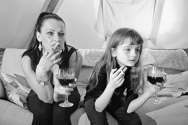 Bad role model mother with daughter "Mother or childminder sitting on couch with a little girl, both of them smoking and drinking a glass of wine while watching an offscreen TVMore like this" little girl smoking cigarette stock pictures, royalty-free photos & images