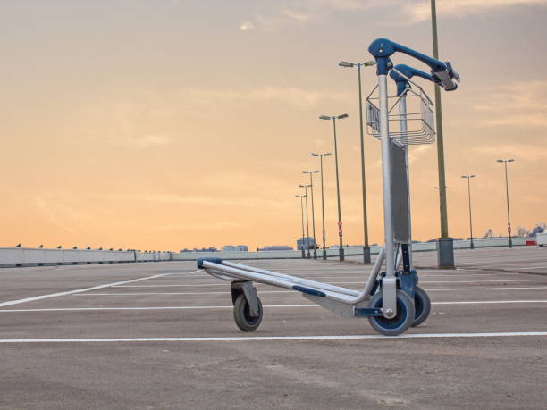 Baggage Cart on empty park deck Luggage cart on empty parking lot at an airport during corona virus covid crisis lockdown in front of orange sky luggage cart stock pictures, royalty-free photos & images