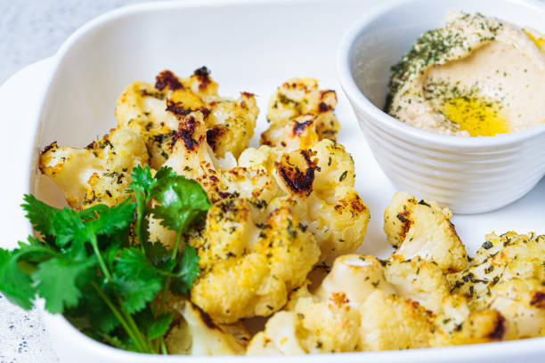 Baked cauliflower in white dish with hummus. Healthy food concept. stock photo