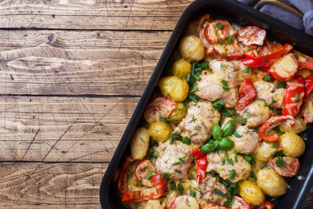 Baked chicken thighs, potatoes and vegetables in a baking tray on a wooden table. Copy space. Baked chicken thighs, potatoes and vegetables in a baking tray on a wooden table Copy space. baking sheet stock pictures, royalty-free photos & images