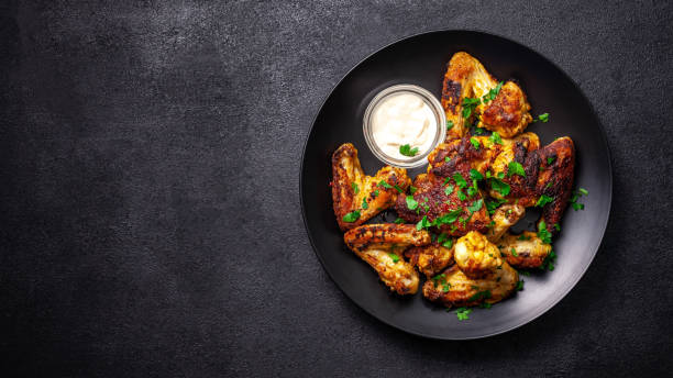 Baked chicken wings in Mexican with curry seasoning and parsley on a black plate, on a black background. side view, copy space, top view stock photo