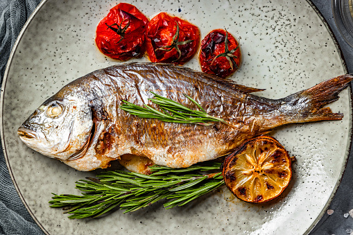 Baked dorado fish on a plate with vegetables top view. High quality photo