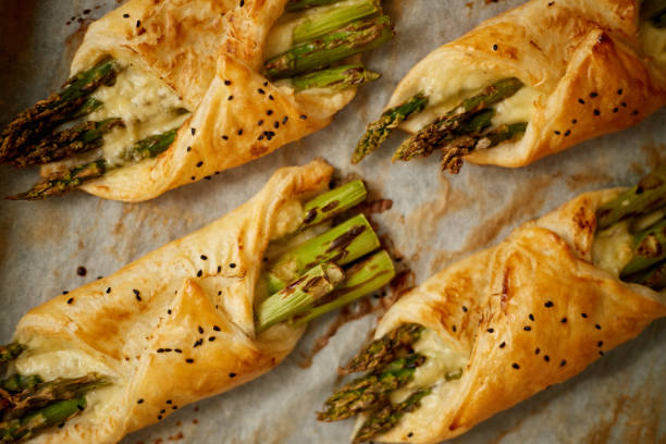 Baked green asparagus in puff pastry sprinkled with sesame seeds. Placed on a white baking paper stock photo