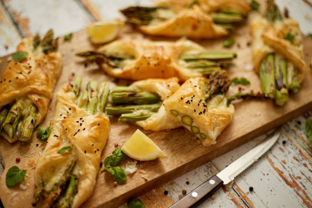 Baked green asparagus wrapped in puff pastry. Served on wooden board. With selective focus stock photo