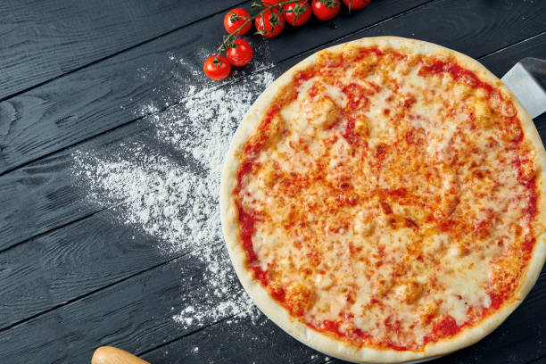 Baked margarita pizza with tomatoes and melted cheese, red sauce and on a black wooden background in a composition with ingredients. Top view stock photo