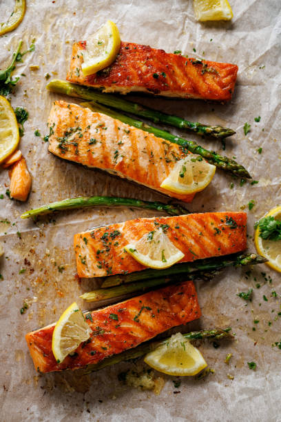 Baked salmon and green asparagus with aromatic herbs and lemon slices on baking paper top view stock photo