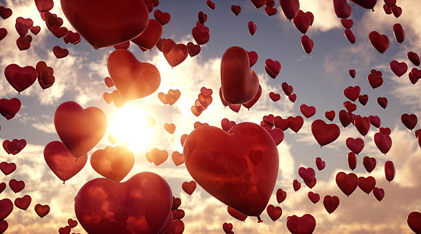 A group of heart-shaped balloons flying through the air on a cloudy sky background. The hearts appear transparent in a red hue and have a slightly marbled surface.